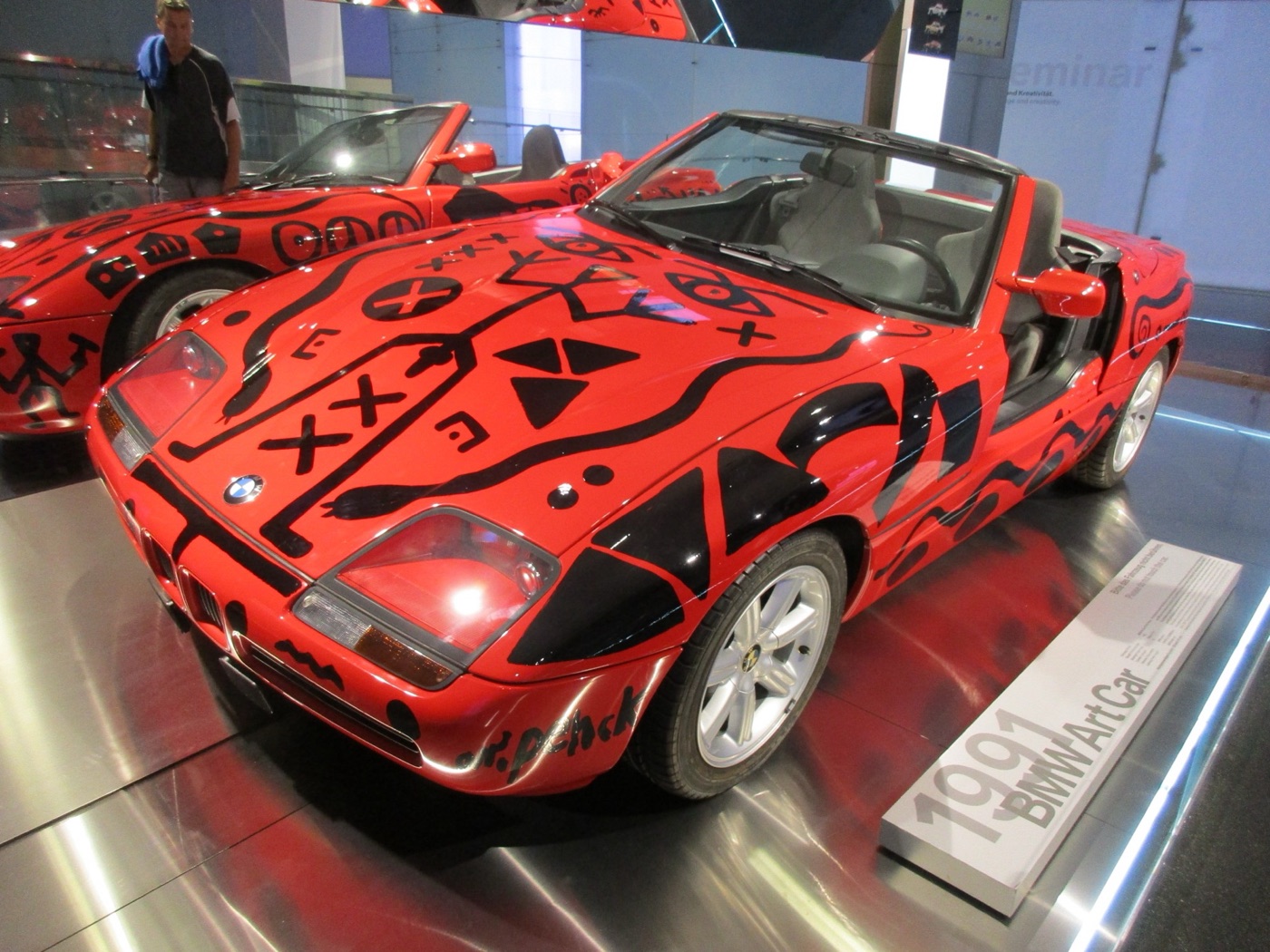 A.R. Penck’s red BMW Z1 Art Car covered in black figures and symbols, beside a plaque reading 1991 BMW Art Car, in the BMW Museum