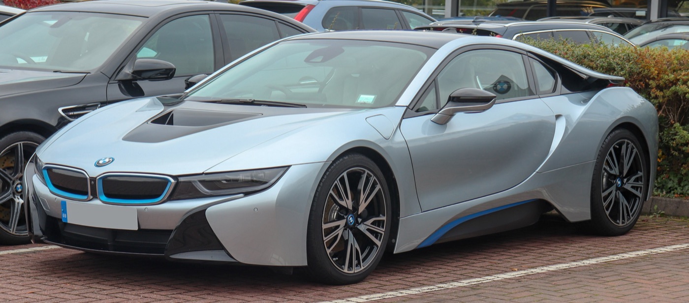 Silver BMW i8 coupé with blue accents and black wheels, front three-quarter view on a car park