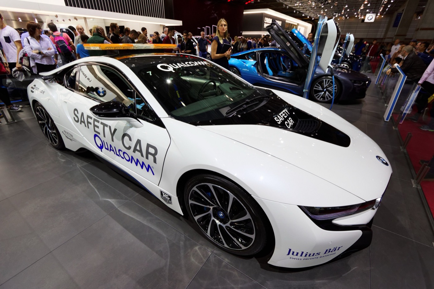 White BMW i8 in Formula E safety car livery with Qualcomm lettering and a light bar on the roof, at a motor show