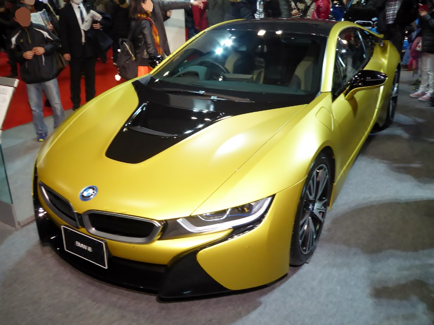 Matt yellow BMW i8 Protonic Frozen Yellow Edition with a black bonnet section, front three-quarter view at a motor show