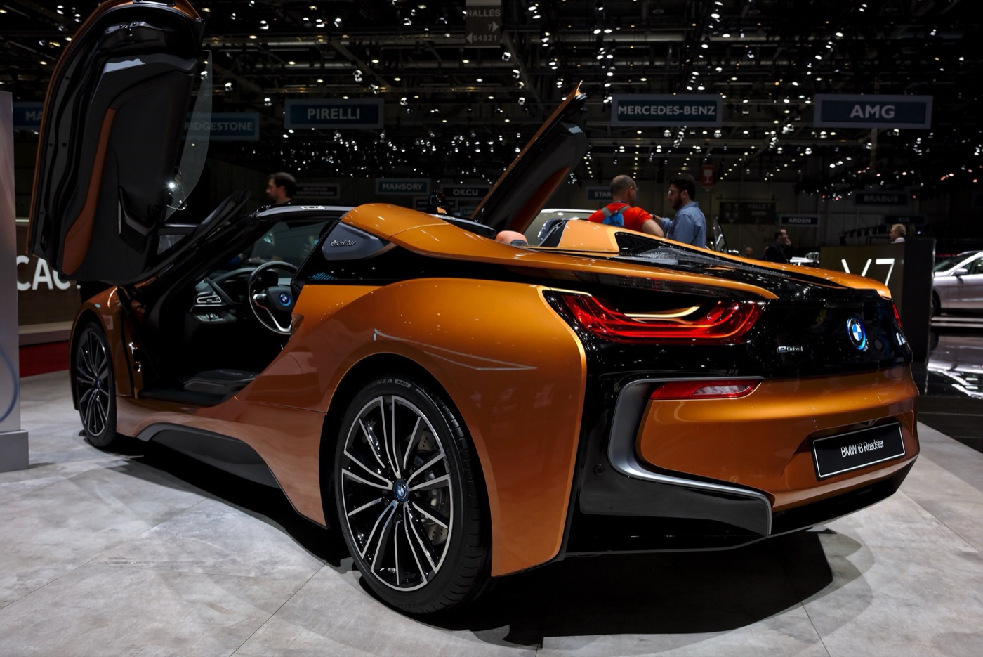 Copper-coloured BMW i8 Roadster with its roof folded and both doors raised, seen from the rear three-quarter on a motor show stand