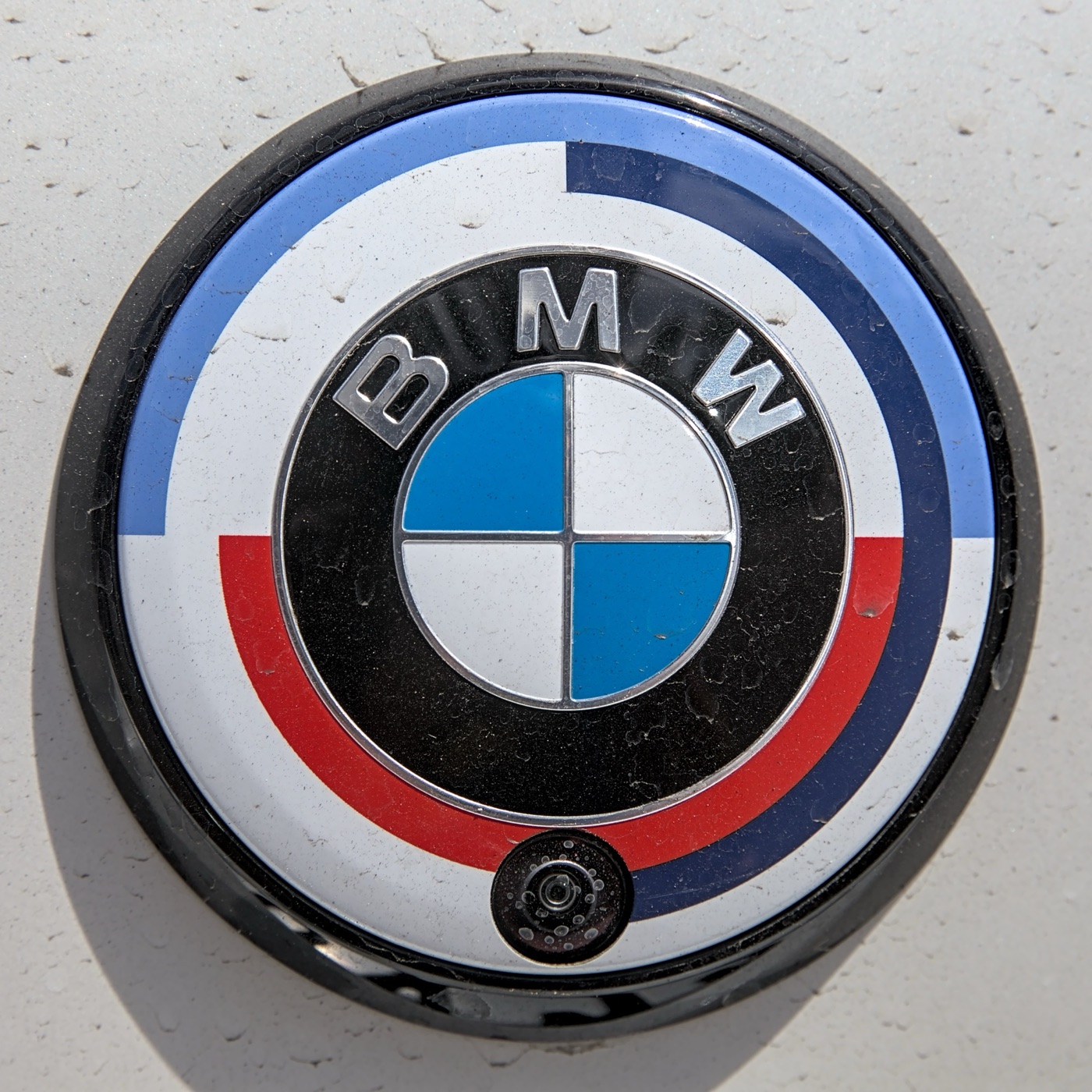 Close-up of a BMW roundel ringed by light blue, dark blue and red semicircles on a white background, fitted to a white car