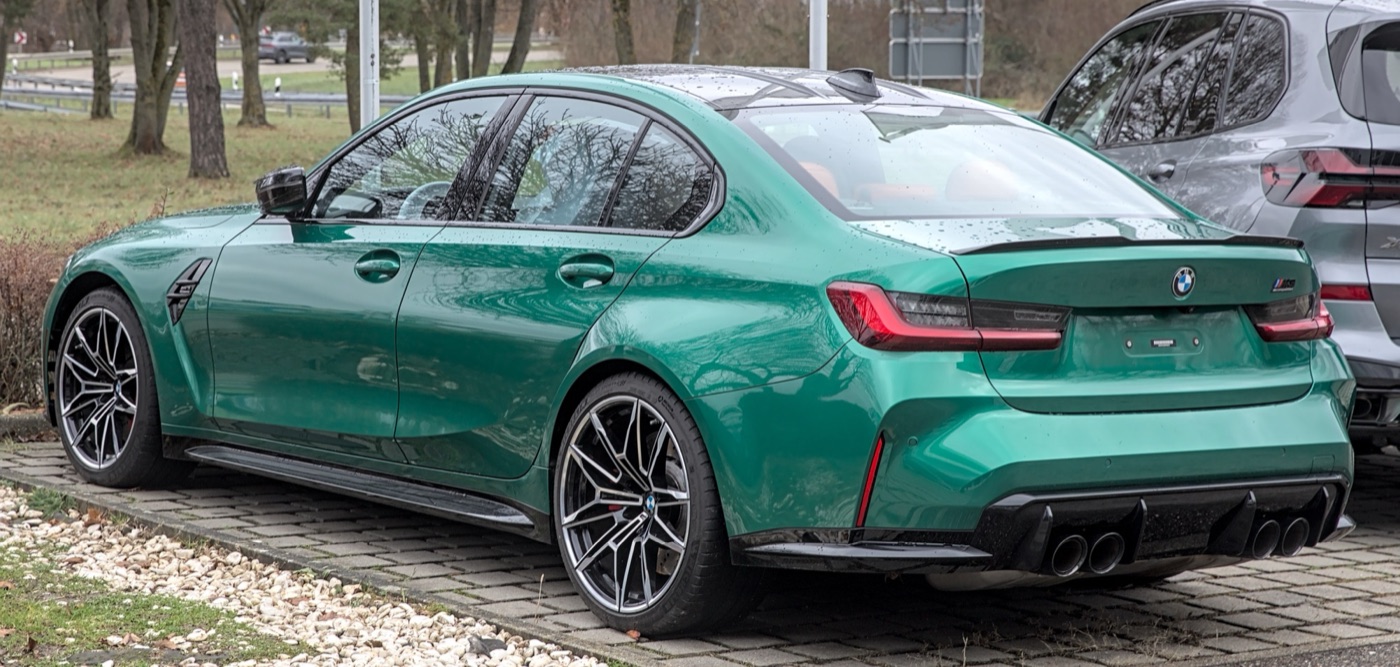 Green BMW M3 Competition saloon of the G80 generation from the rear three-quarter, with four exhaust tips and a carbon boot spoiler