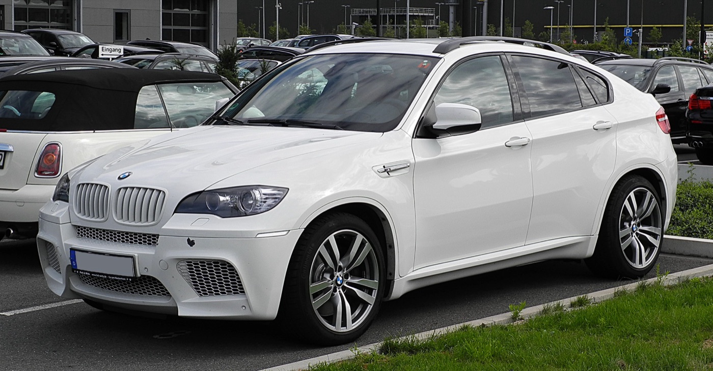 White first-generation BMW X6 M coupe-styled SUV parked in a car park, seen from the front three-quarter with a mesh-filled front bumper