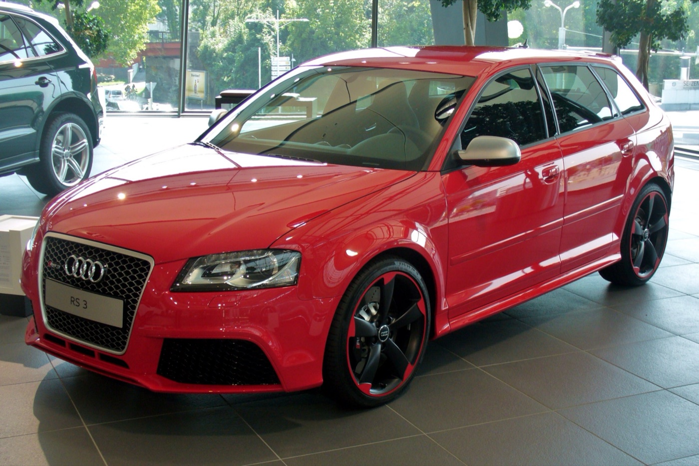 Red 2011 Audi RS3 Sportback with black and red alloy wheels in a showroom