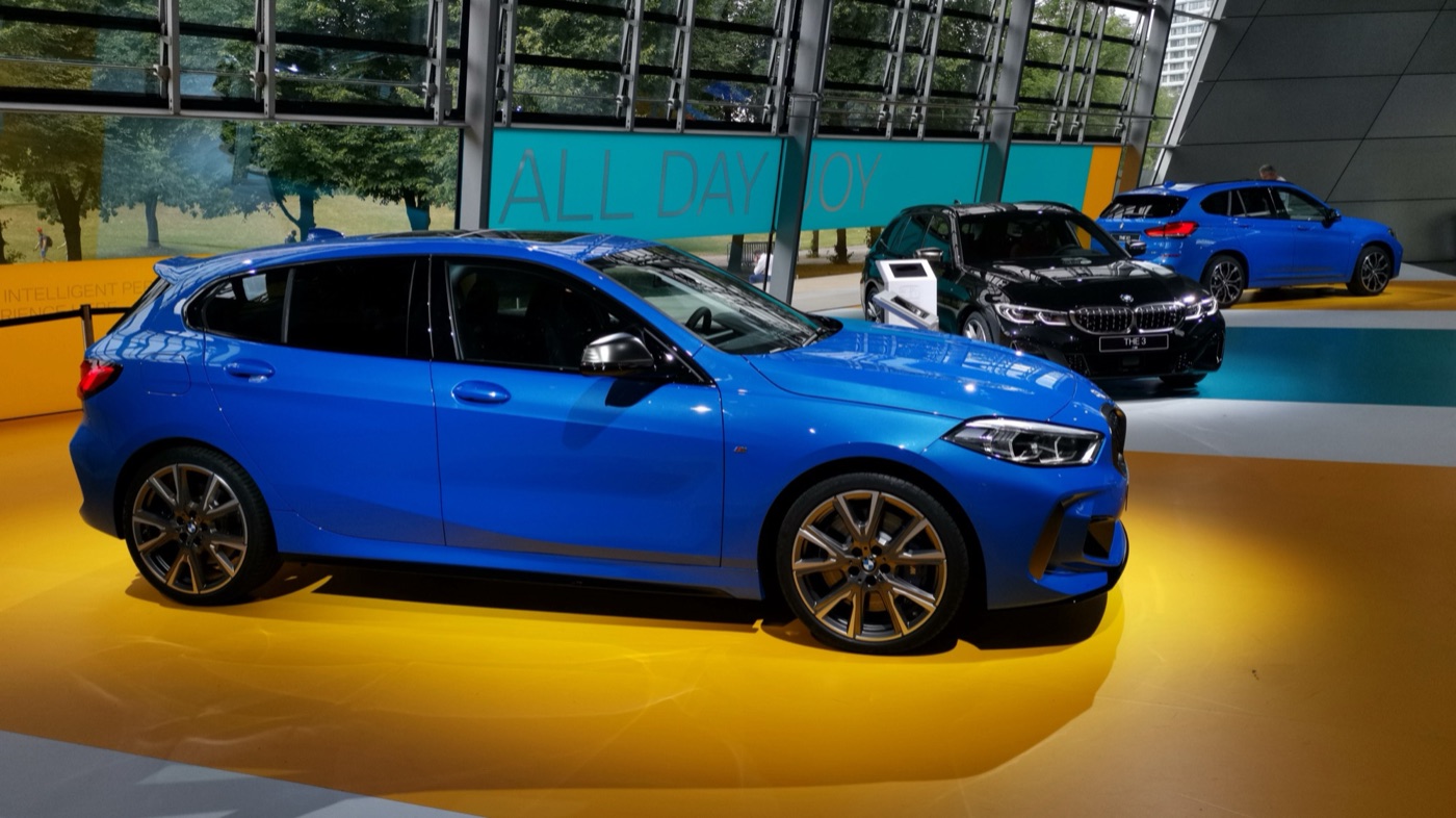Blue BMW M135i xDrive five-door of the F40 generation on a yellow display floor, seen from the side