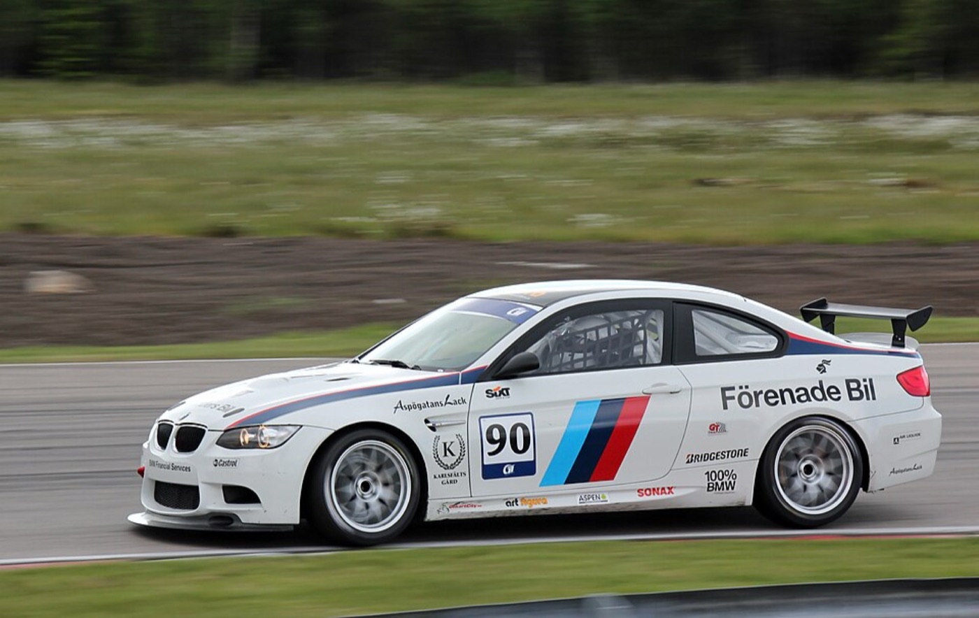White BMW M3 GT4 racing car with number 90 and Motorsport stripes, at speed on track