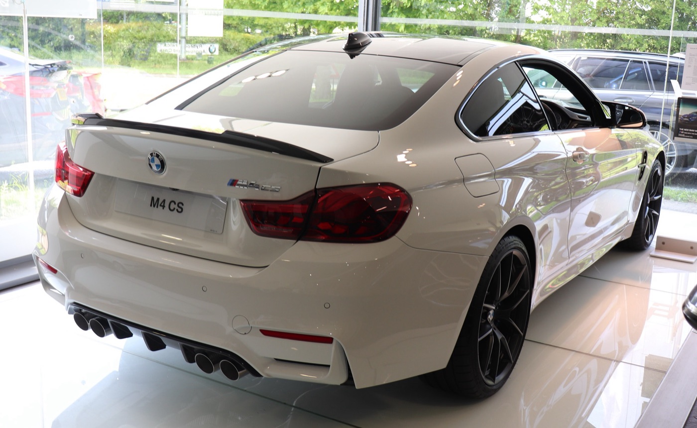 White BMW M4 CS from the rear three-quarters, showing the carbon boot-lid spoiler, OLED tail lights and four tailpipes