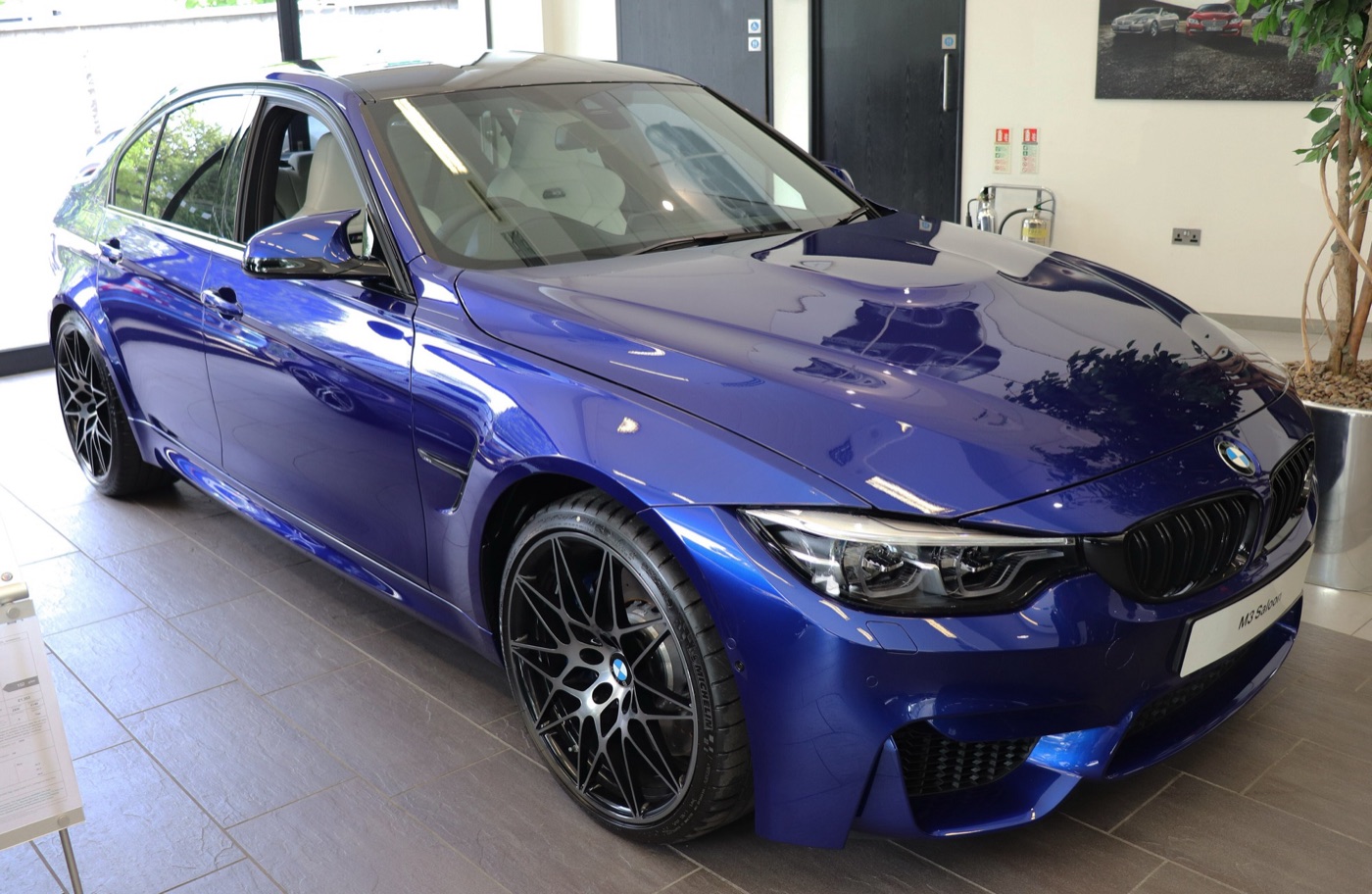 Dark blue F80 BMW M3 Competition saloon with black 20-inch wheels in a showroom
