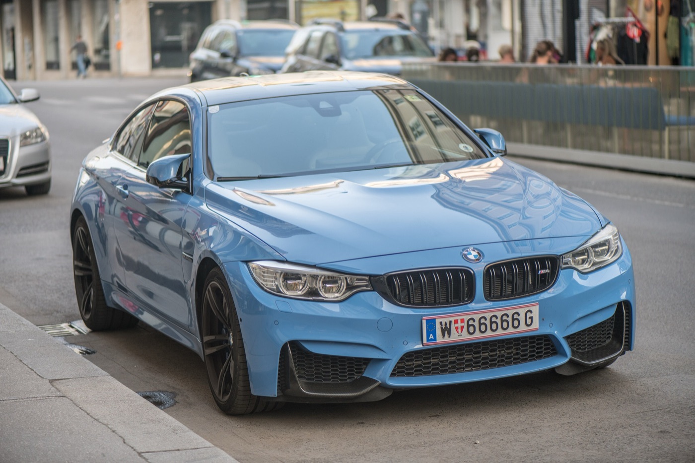 Light-blue BMW F82 M4 Coupe with black wheels and carbon roof parked at a kerb