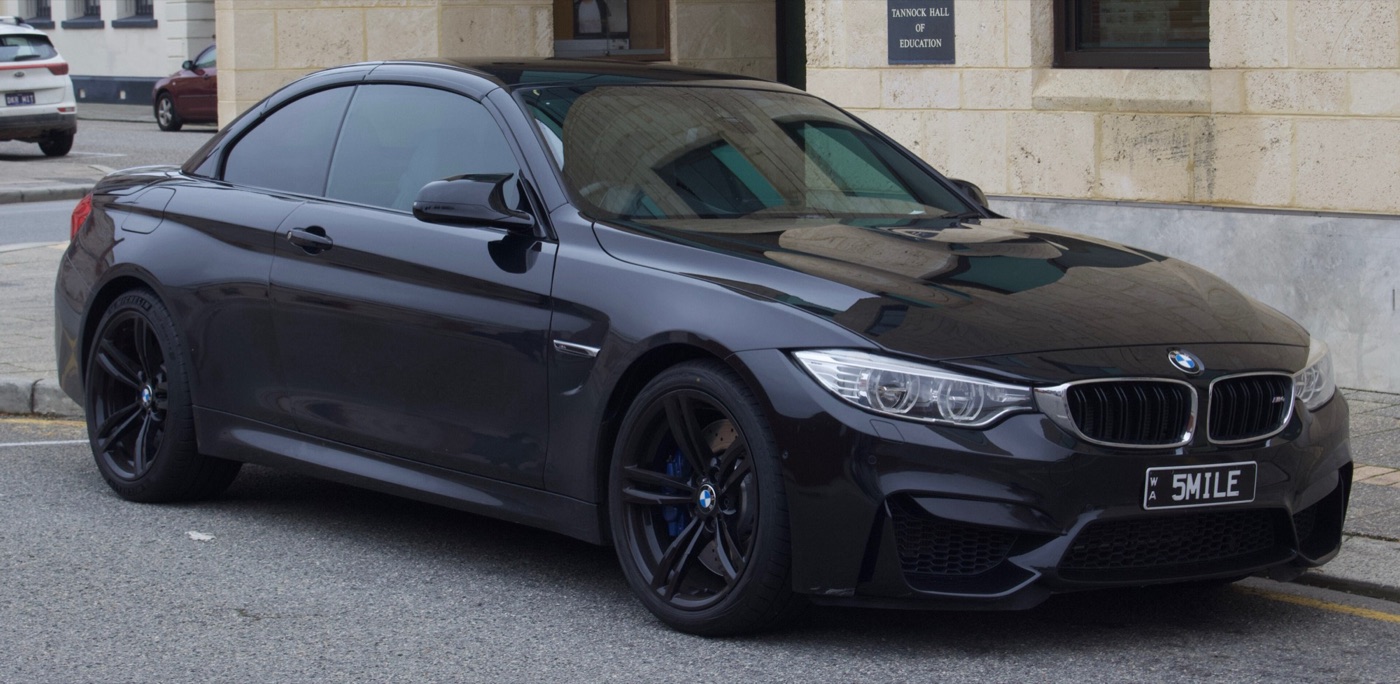 Black F83 BMW M4 Convertible with its folding hard top closed, parked on a street