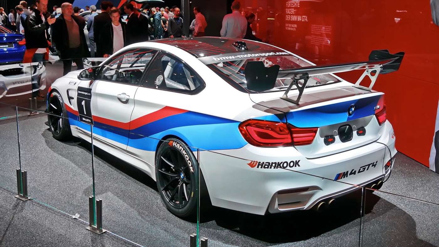 White BMW M4 GT4 racing car in BMW M livery with a large rear wing on a show stand