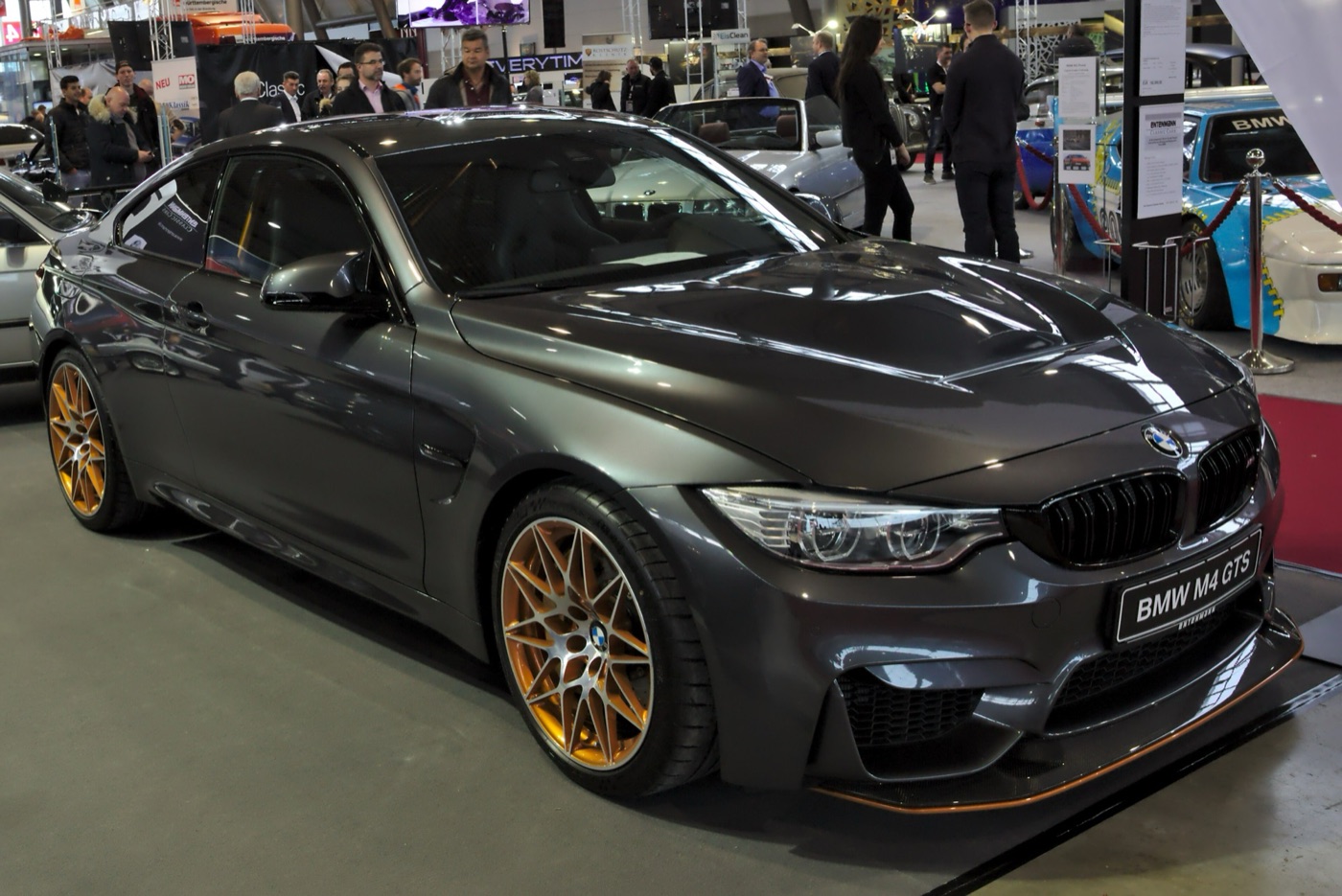 Dark grey BMW M4 GTS with orange wheels and an orange-edged front splitter on a show stand