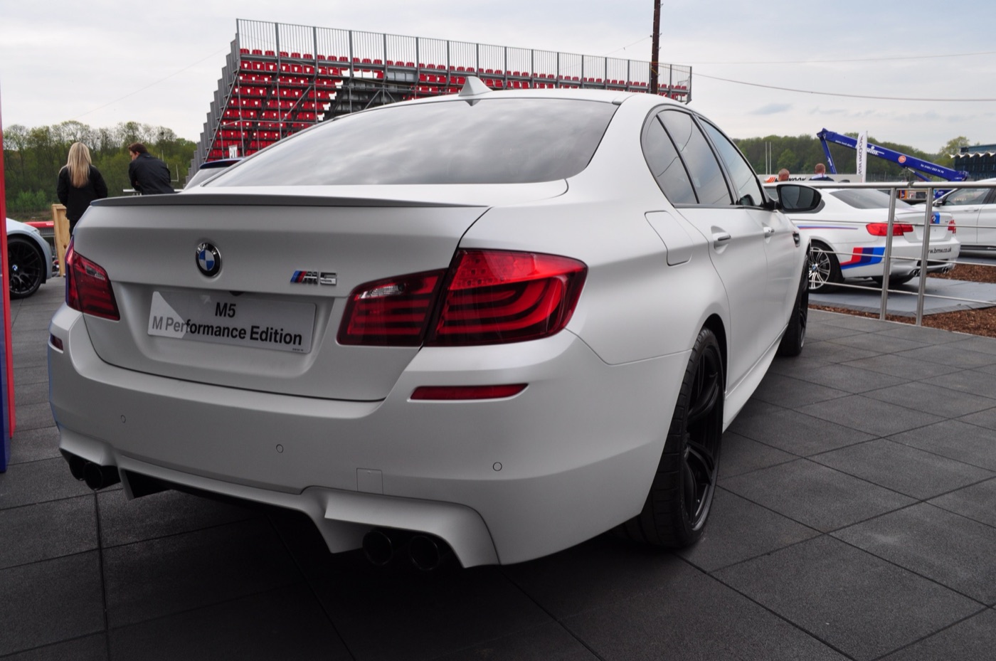Matt white BMW M5 F10 from the rear with black wheels and an M5 M Performance Edition placard, on a display at a racing circuit