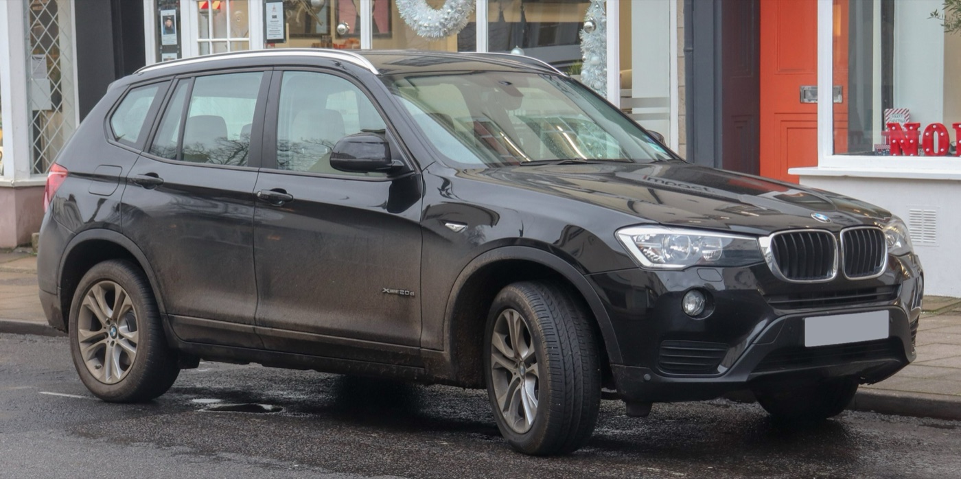 Black facelifted BMW X3 xDrive20d SE with muddy sides parked on a wet high street