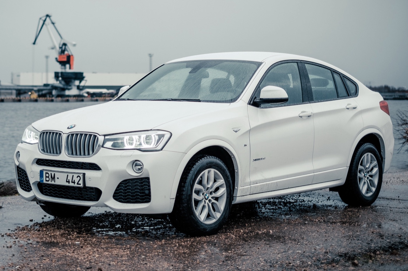 White BMW X4 F26 parked on a wet quayside with cranes behind, seen from the front three-quarter