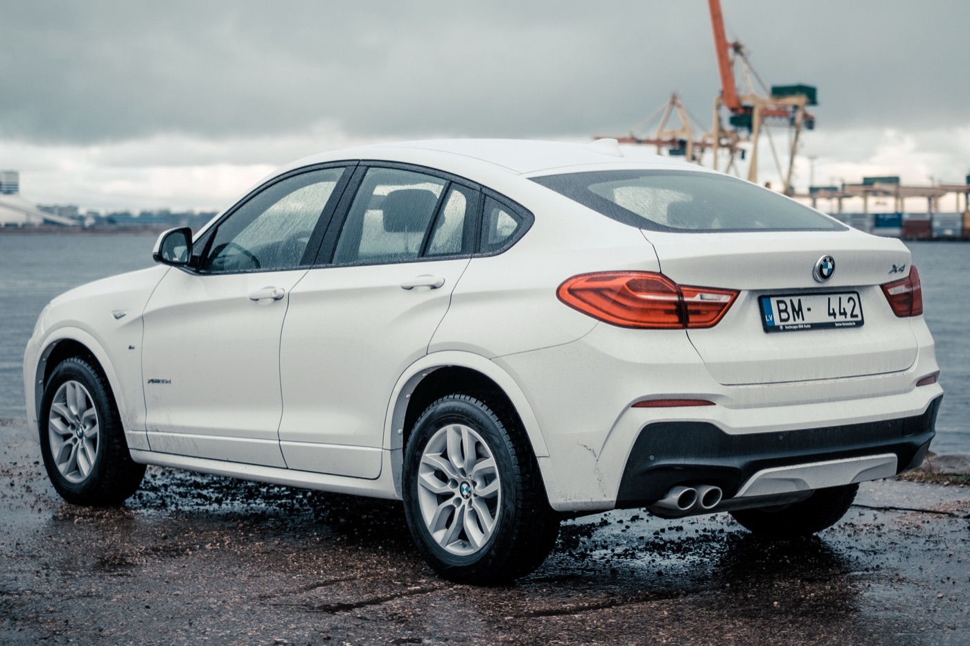 White BMW X4 F26 seen from the rear three-quarter on a wet quayside, showing the sloping roof and L-shaped tail lights