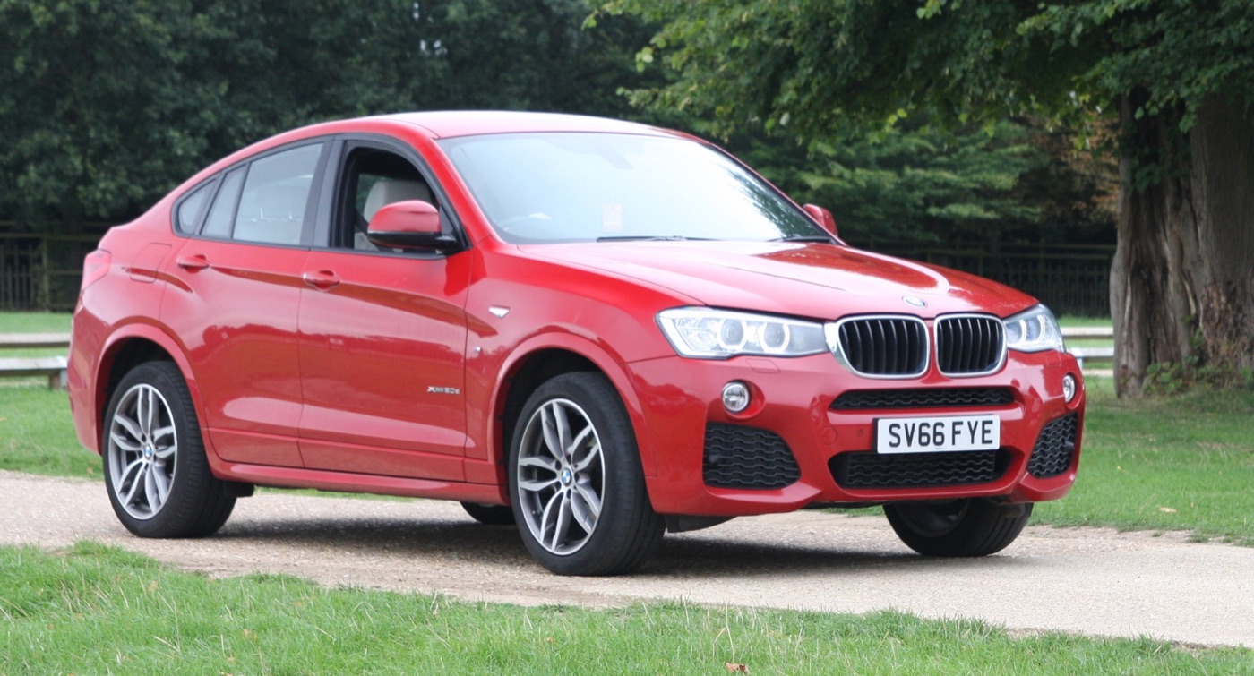 Red BMW X4 xDrive20d on a UK registration plate parked on a gravel drive beside grass and trees
