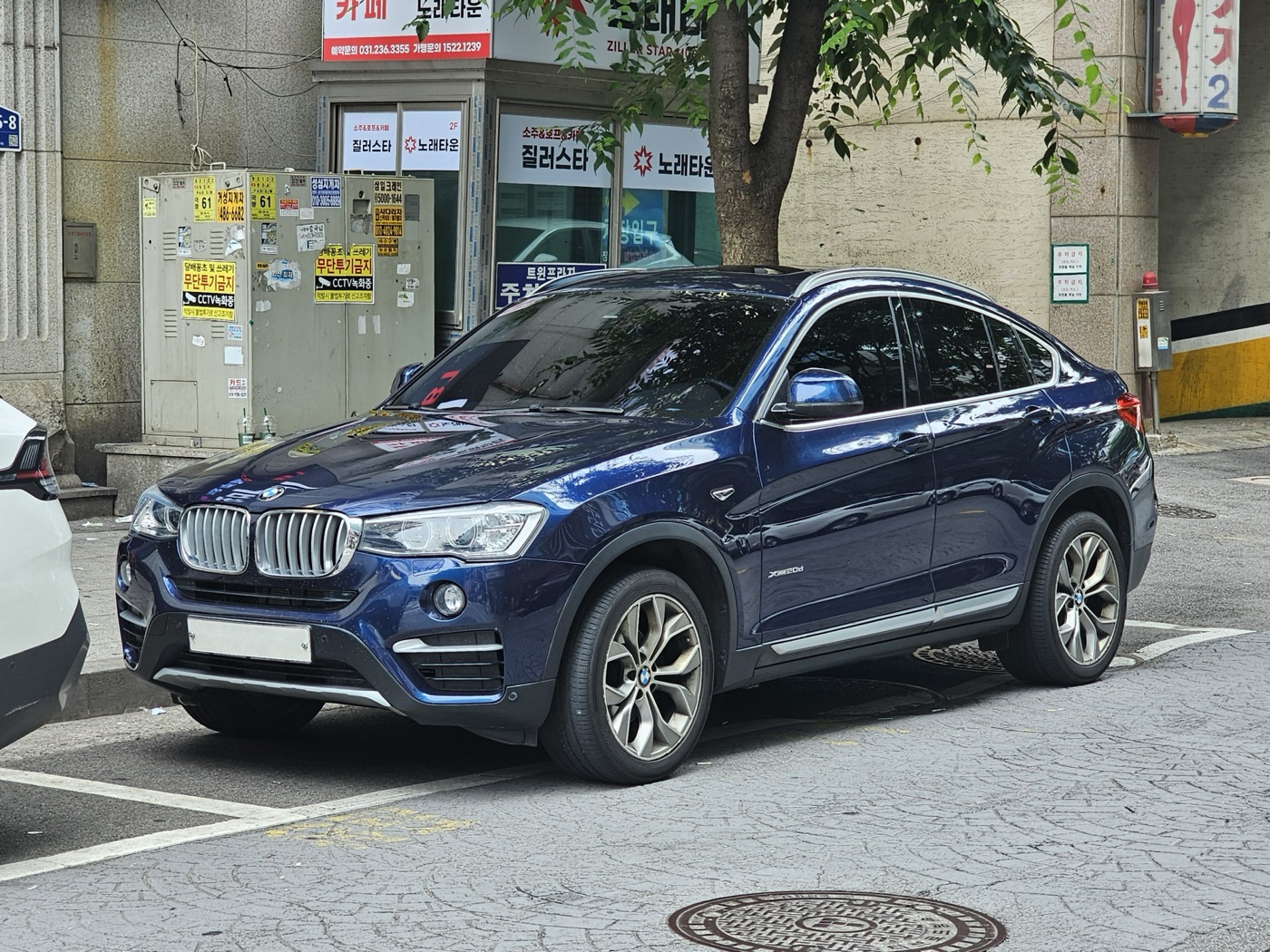 Dark blue BMW X4 F26 xDrive20d xLine parked on a city street, seen from the front three-quarter