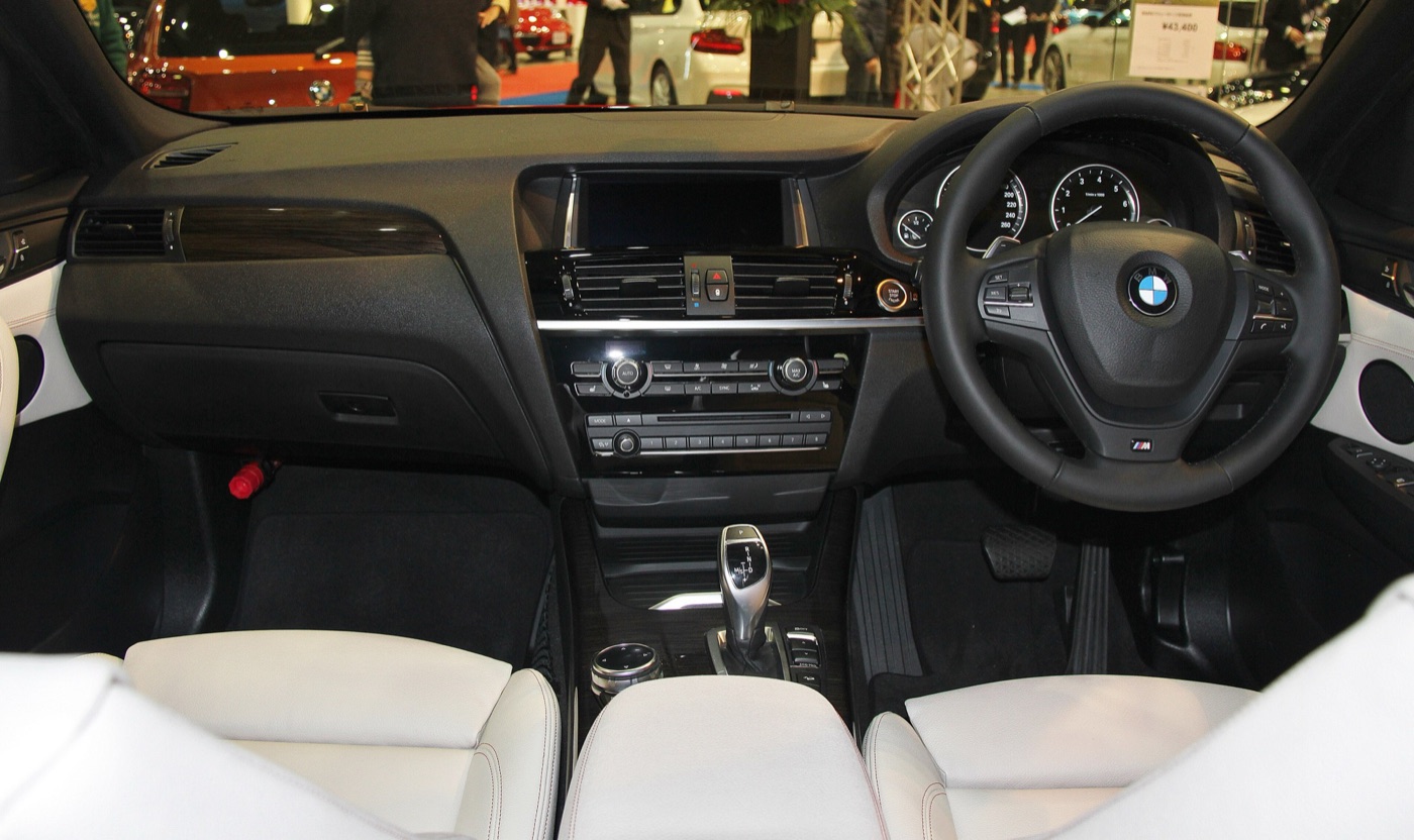 Dashboard of a right-hand-drive BMW X4 F26 with M steering wheel, iDrive screen and white leather seats