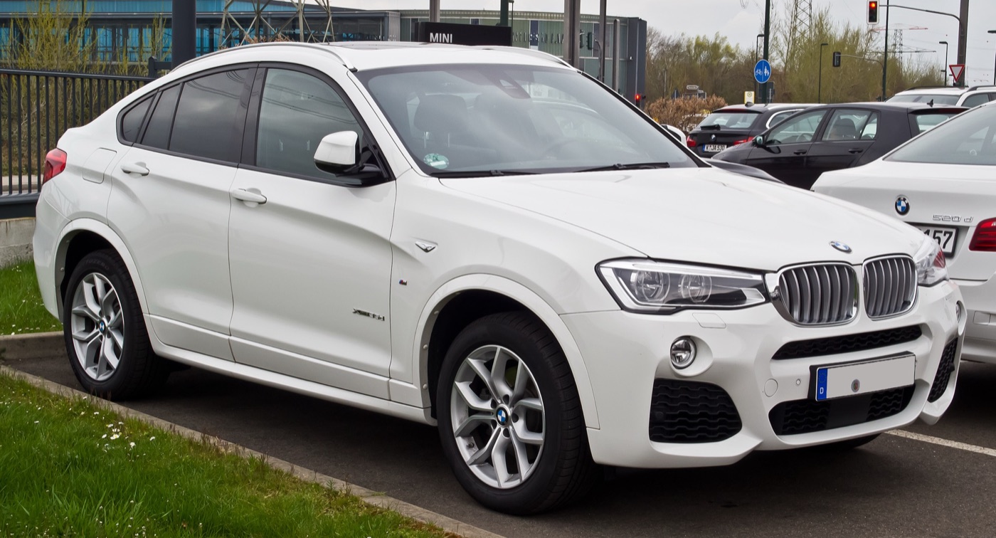 White BMW X4 F26 xDrive35d M Sport parked at a kerb in front of a dealership car park