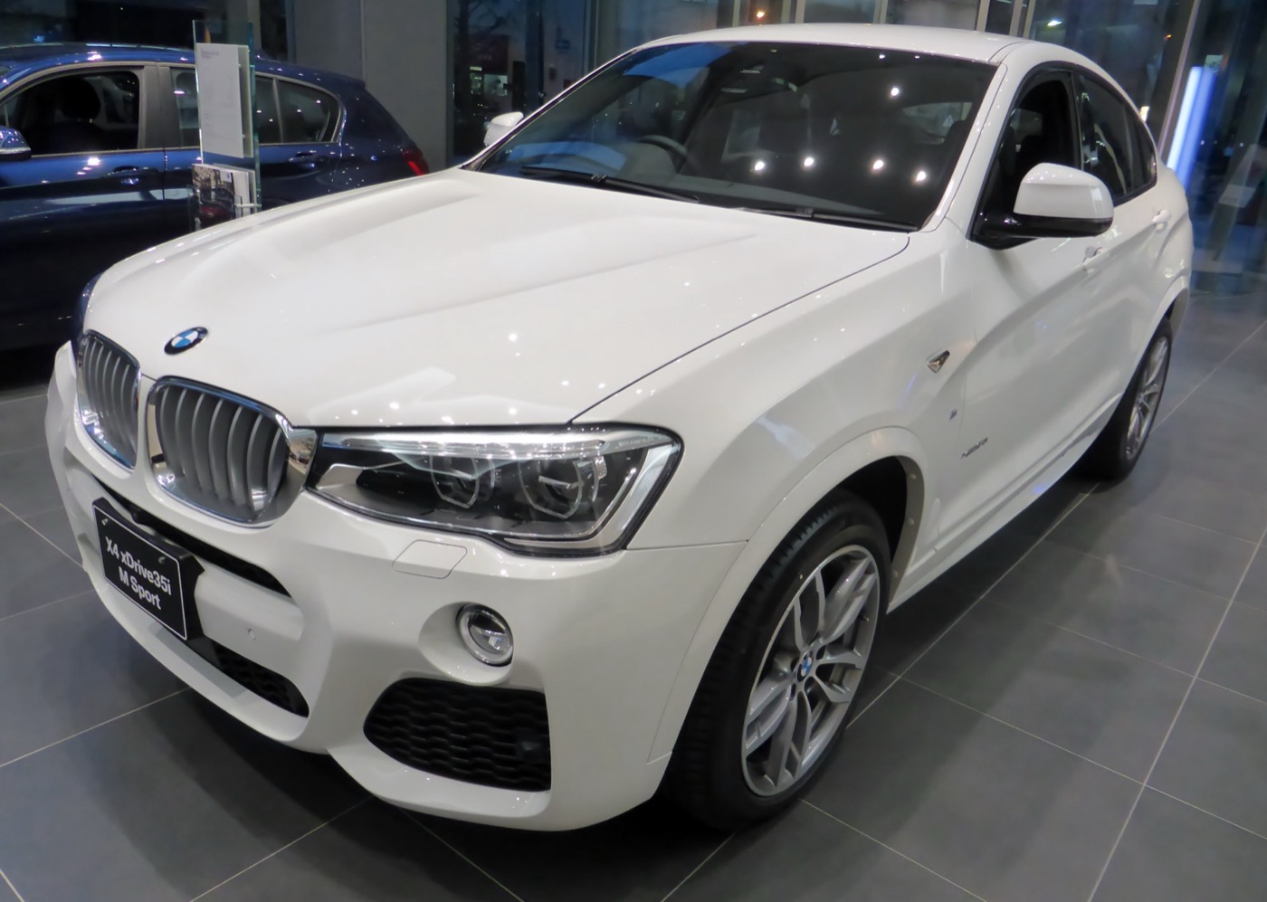 White BMW X4 xDrive35i M Sport in a showroom, front three-quarter view with its model plate on the bumper