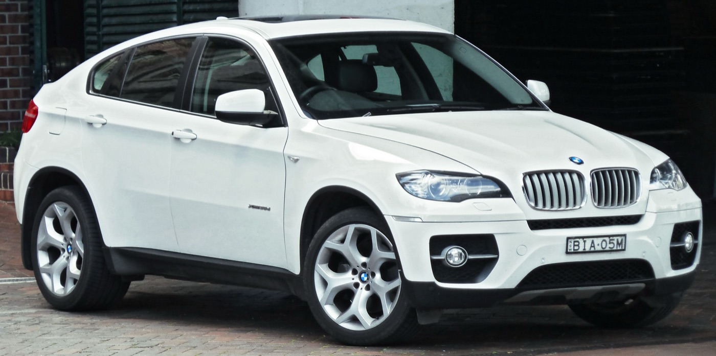 White BMW X6 E71 xDrive35d parked on a brick-paved street, seen from the front three-quarter