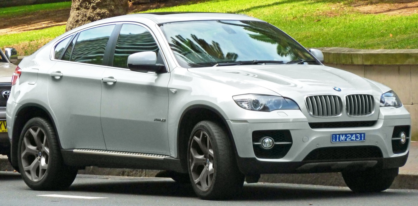 Silver BMW X6 xDrive50i parked at a kerb beside a park, seen from the front three-quarter
