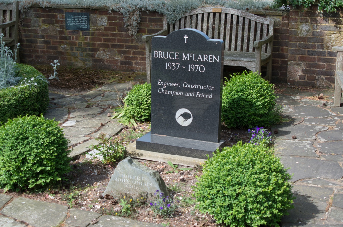 Black headstone reading Bruce McLaren 1937 to 1970, Engineer, Constructor, Champion and Friend, with a kiwi emblem, in a small walled garden