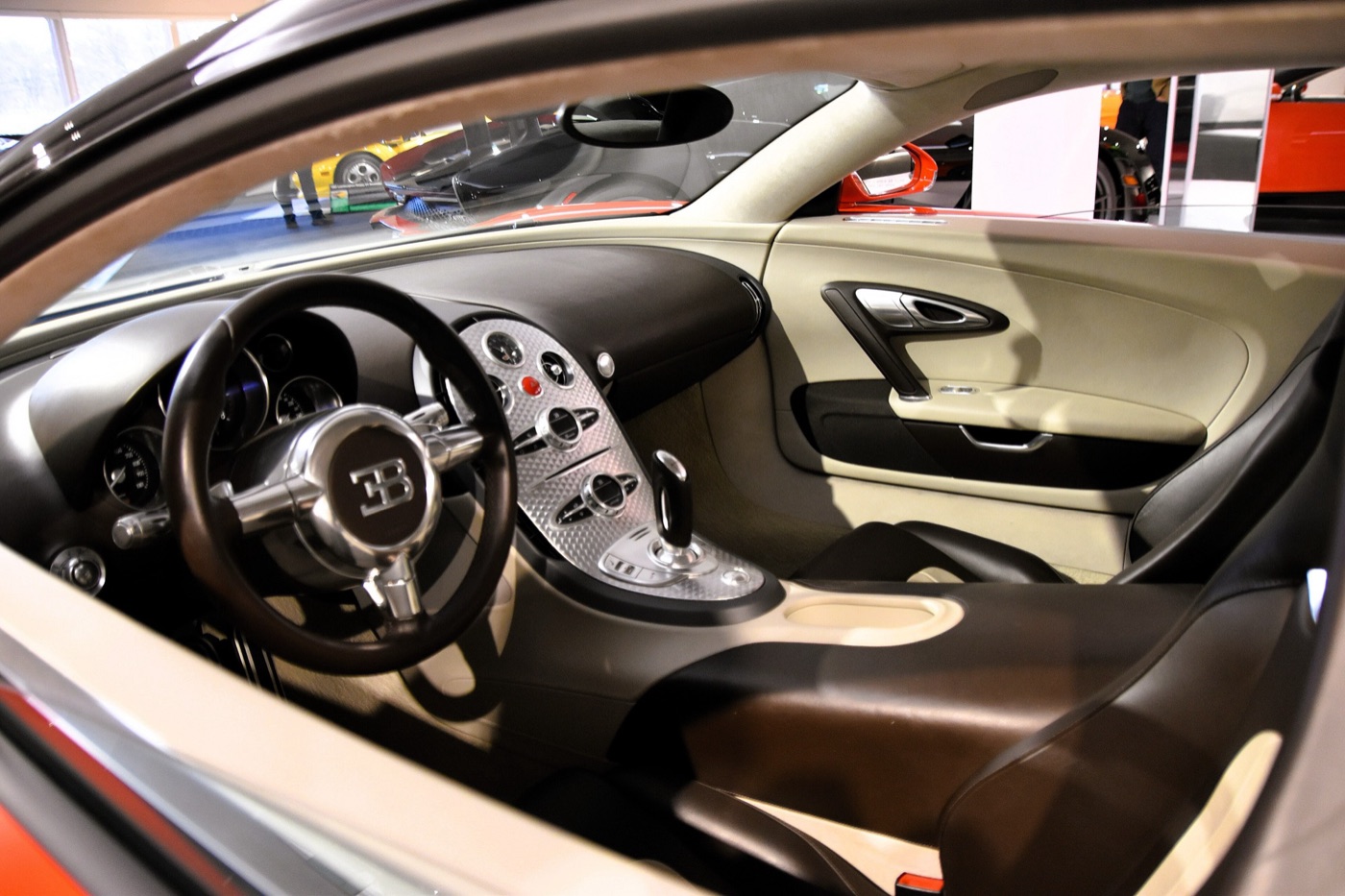 Interior of a Bugatti Veyron with cream and dark brown leather, an EB-badged steering wheel and a polished aluminium centre console with round dials