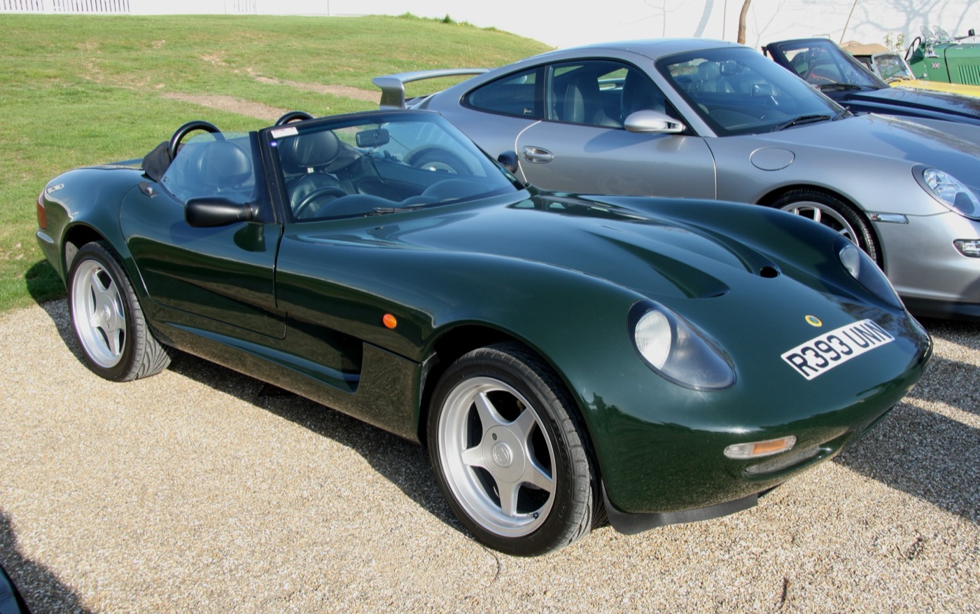 Dark green Caterham 21 roadster with the roof down and five-spoke alloy wheels, parked on gravel