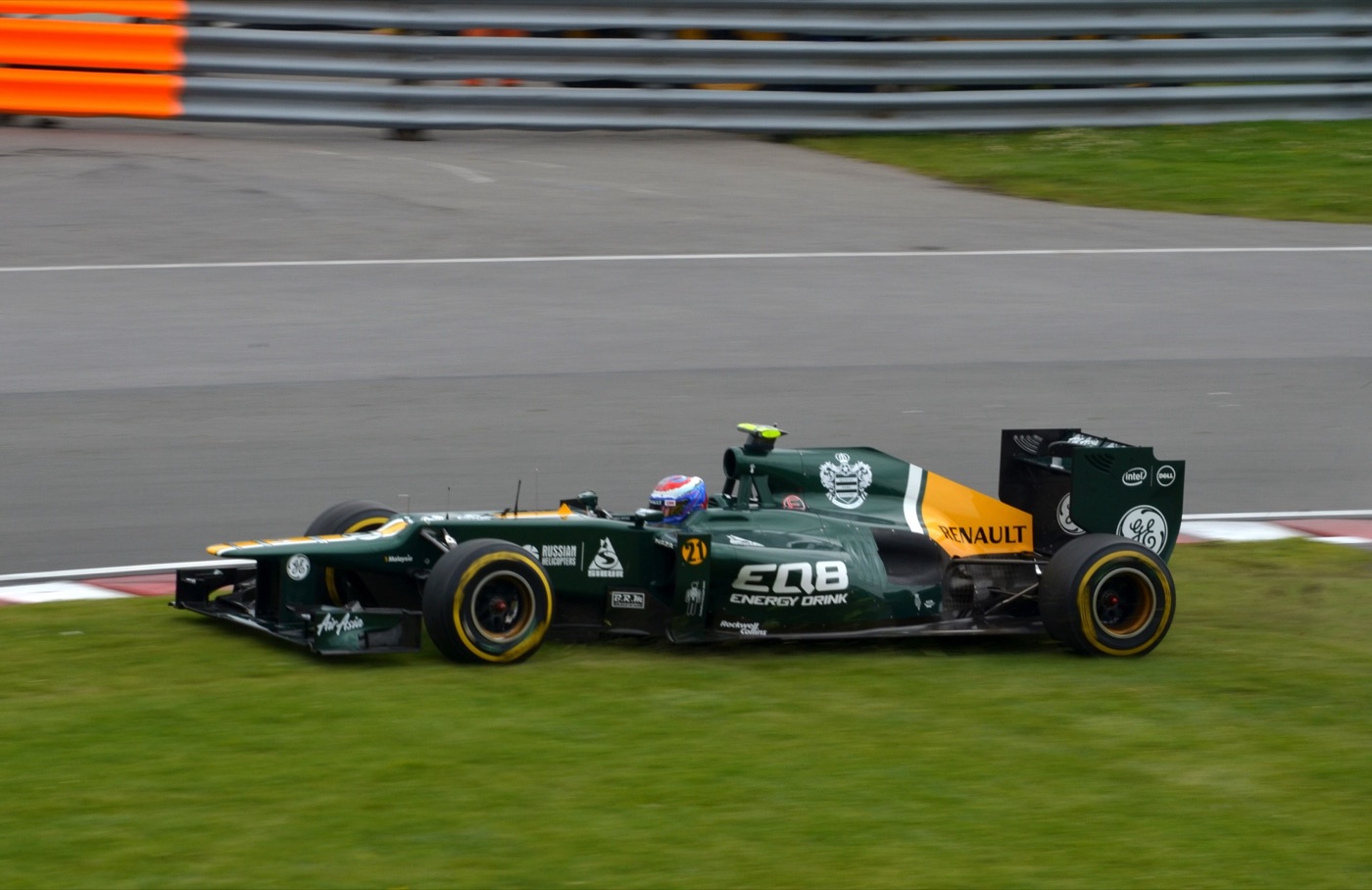 Green and yellow Caterham CT01 Formula One car running wide over the grass at a corner