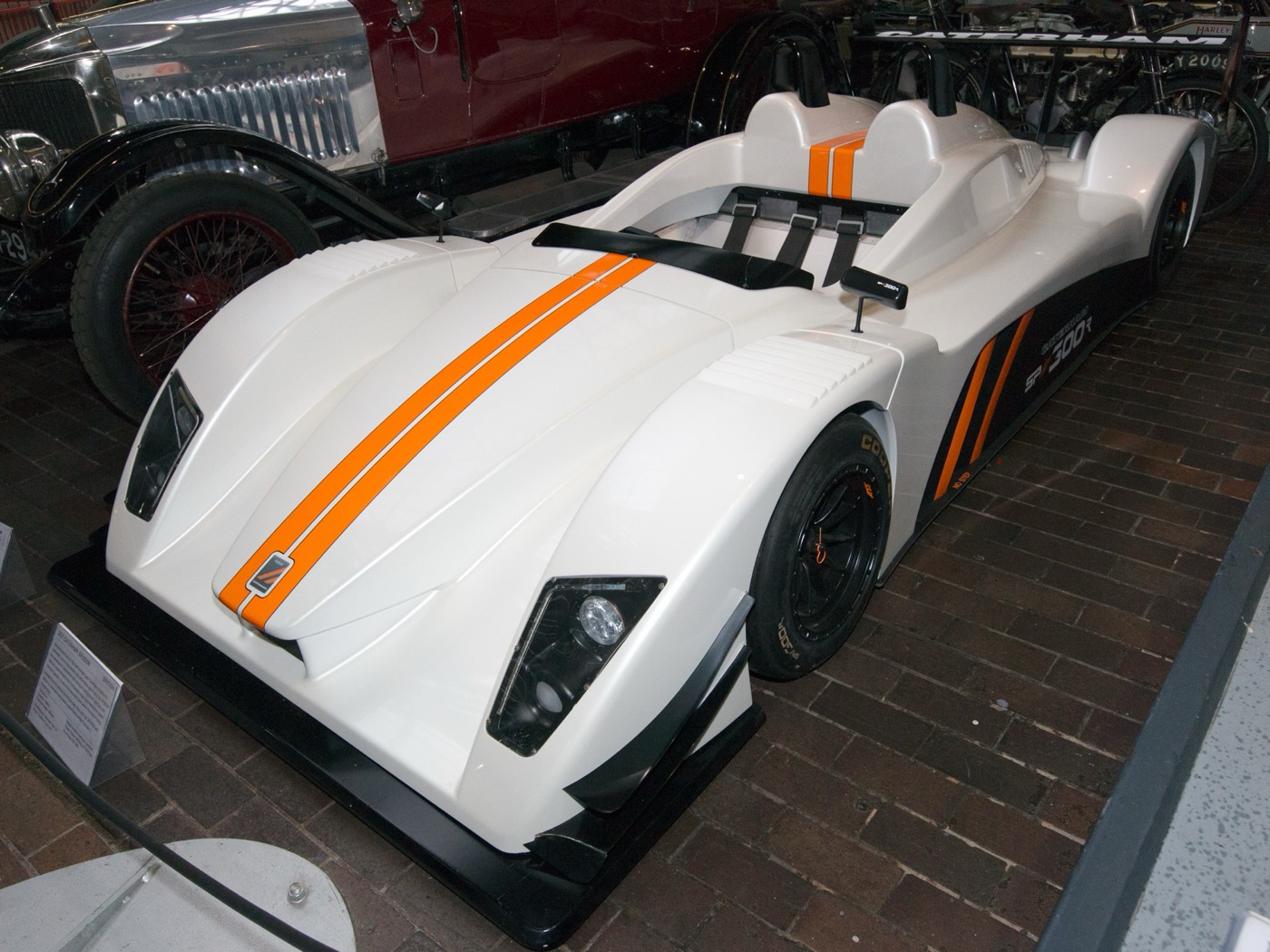 White Caterham SP/300.R sports prototype with twin orange stripes on display in a museum