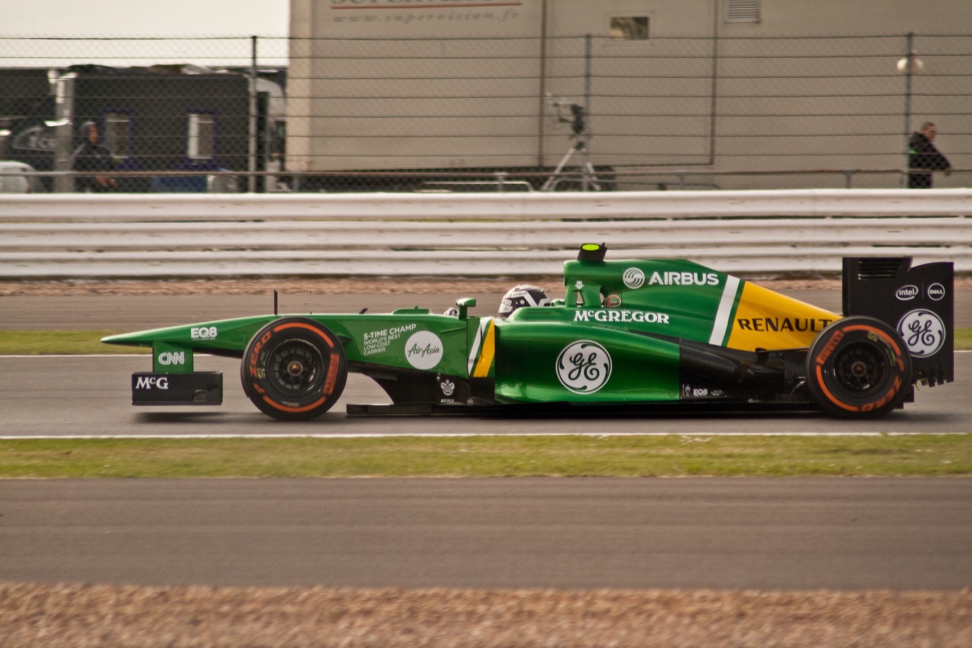 Bright green Caterham CT03 with Airbus, GE and Renault logos passing a pit wall fence, side view