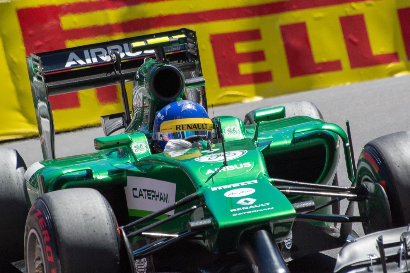 Green Caterham CT05 with a low stepped nose and Airbus rear wing, driver in a blue helmet, passing a Pirelli banner
