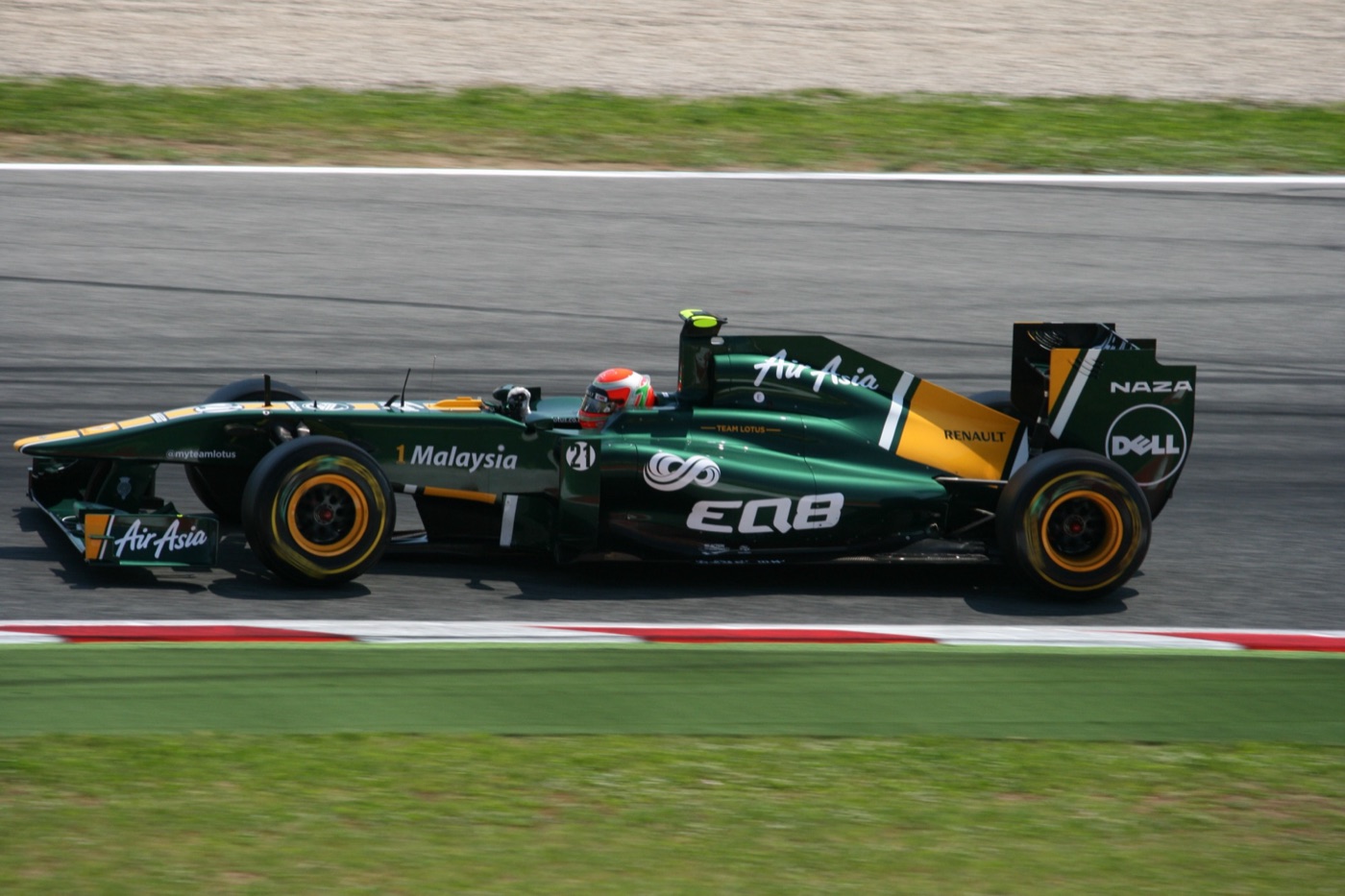 Green Team Lotus T128 Formula 1 car with yellow engine cover and AirAsia logos at speed, side view