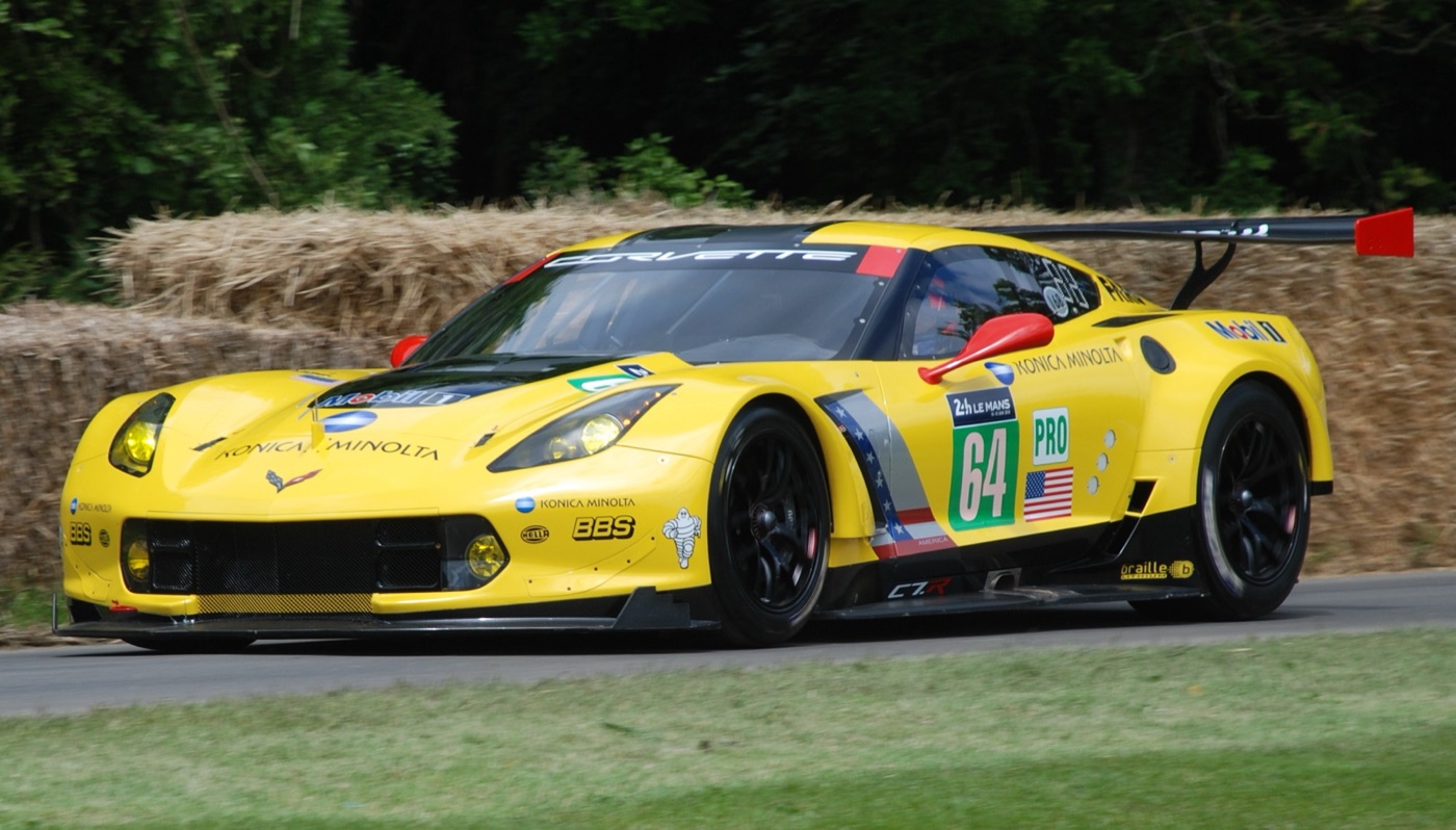 Yellow Corvette C7.R number 64 in Le Mans livery with a large rear wing, driving past straw bales