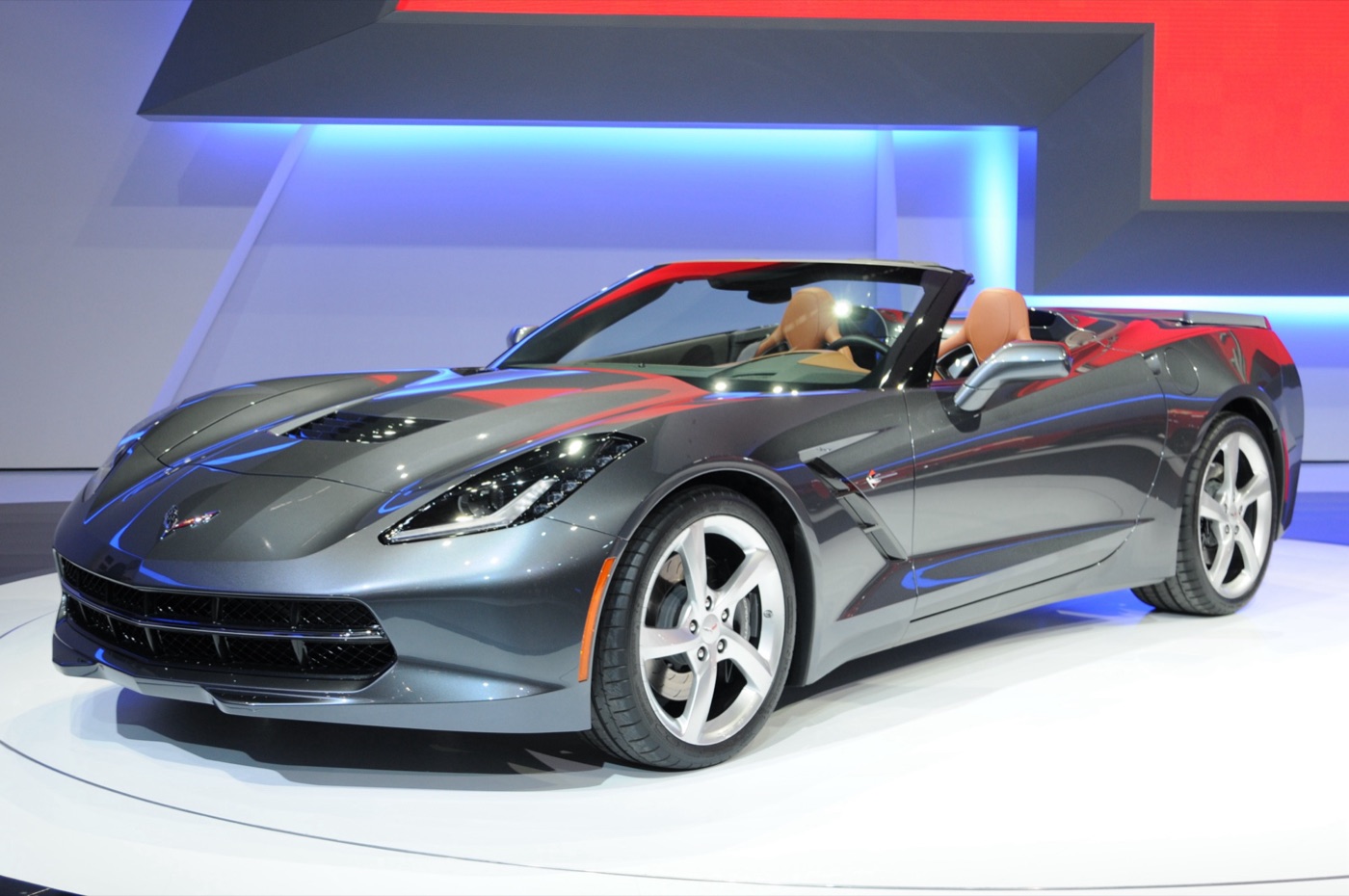 Grey C7 Corvette Stingray convertible with tan leather seats and five-spoke silver wheels on a show stand