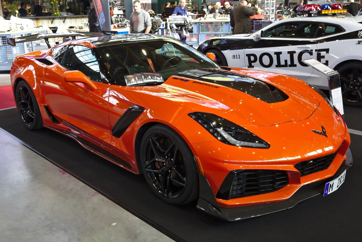 Orange C7 Corvette ZR1 with a carbon rear wing, black wheels and an open bonnet centre, on a show stand