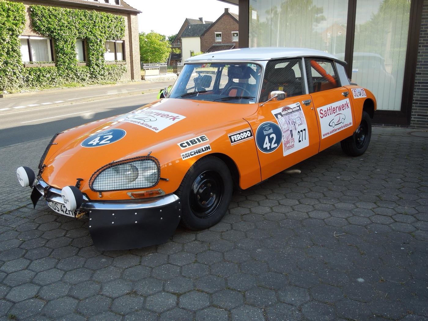 Orange Citroën DS with a white roof prepared for historic rallying, with wire mesh over the headlamps, auxiliary lamps, black wheels and rally number 42