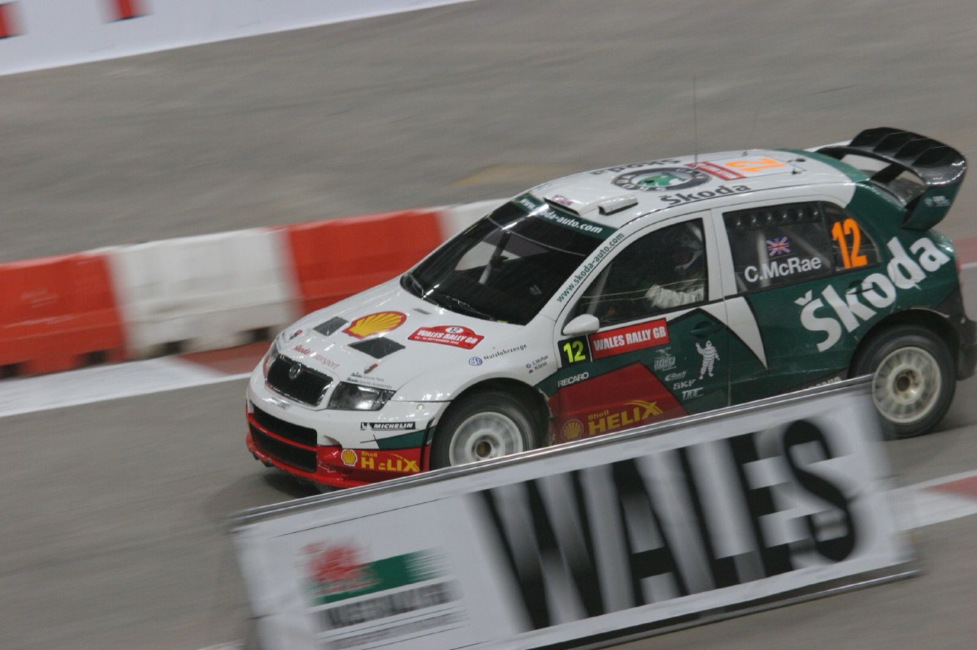 White and green Škoda Fabia rally car with C. McRae on the rear side window, panned at speed on an indoor stage