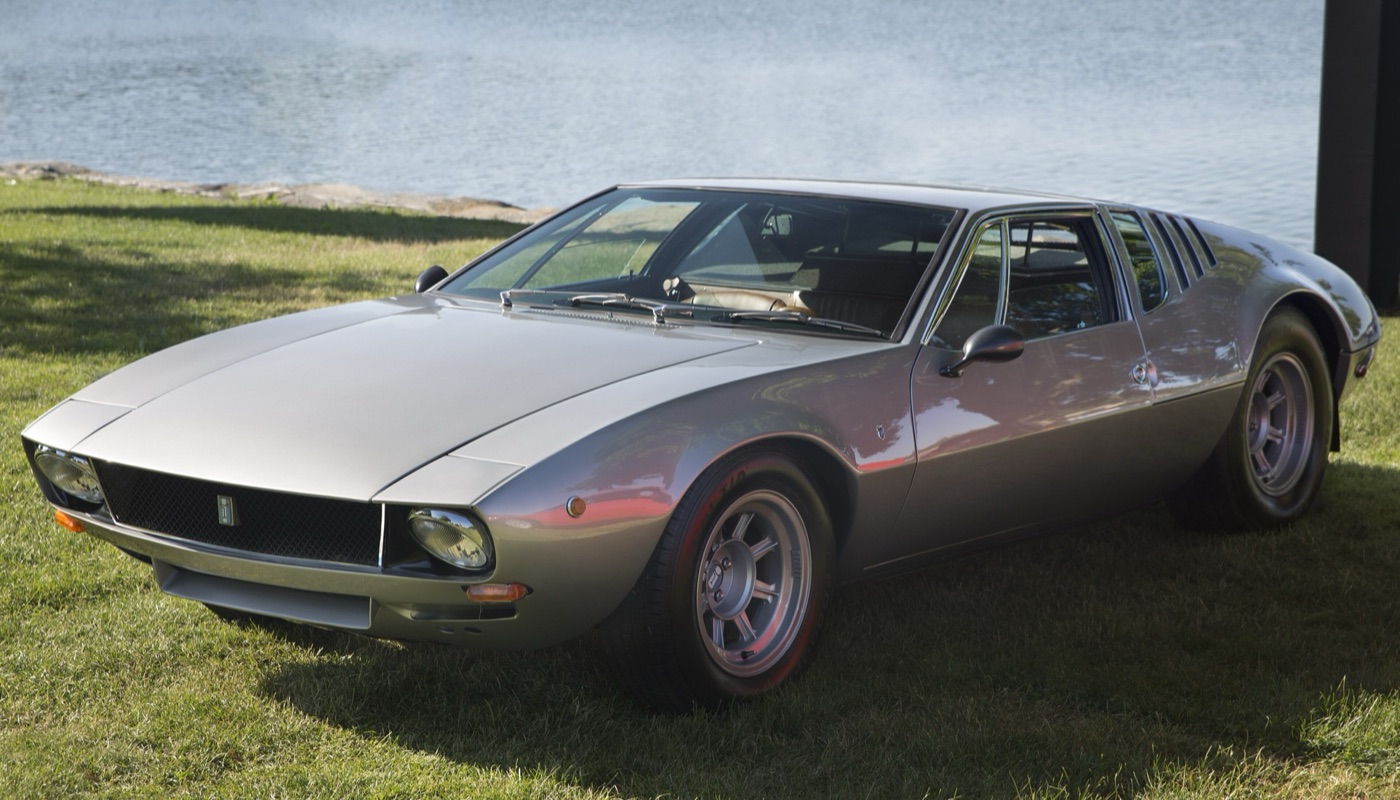 Silver De Tomaso Mangusta coupé, low and wedge-fronted, parked on grass beside water