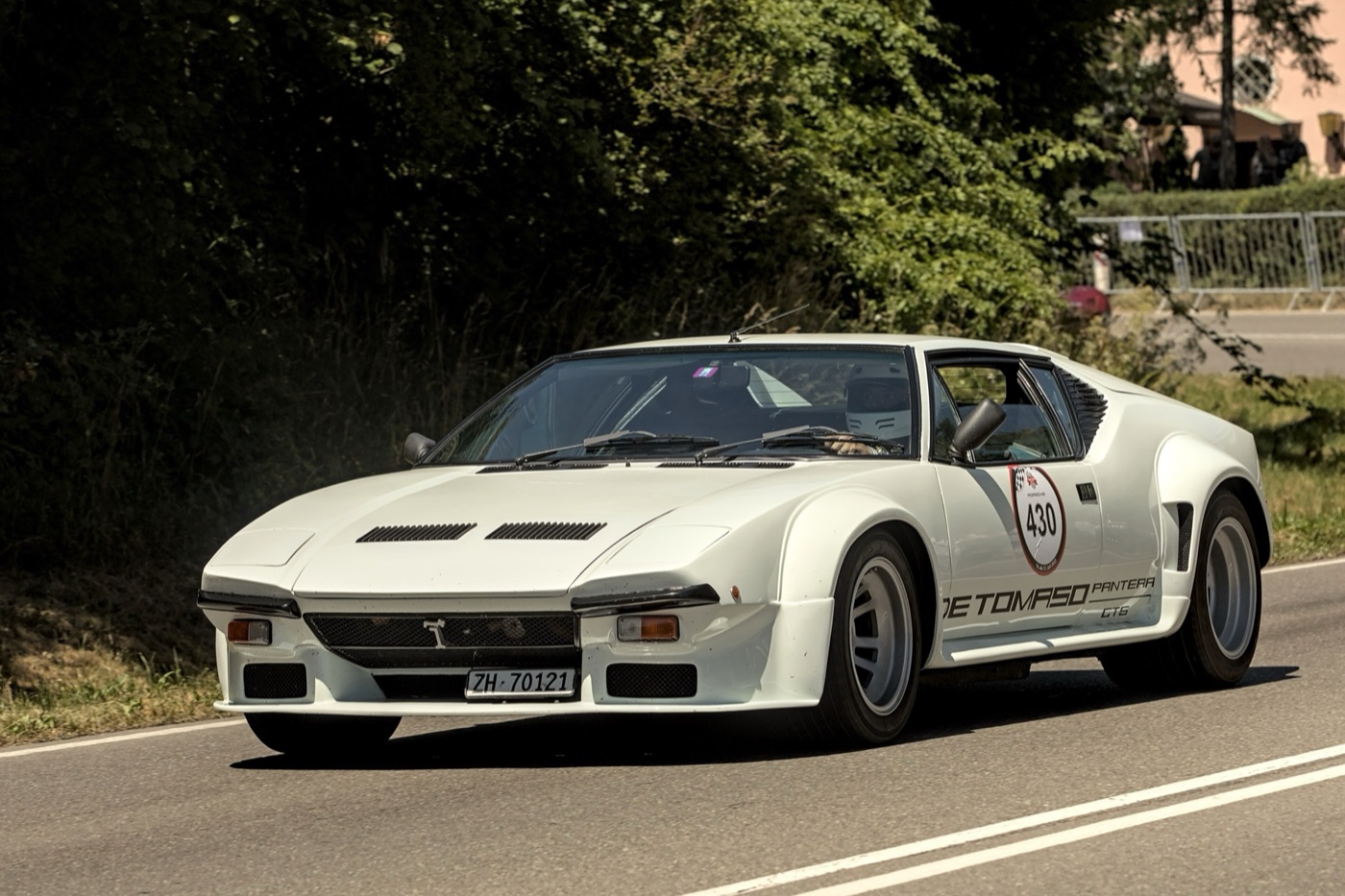 White De Tomaso Pantera GT5 with flared wheel arches and De Tomaso Pantera lettering on the sill, driving on a country road with a rally number on the door