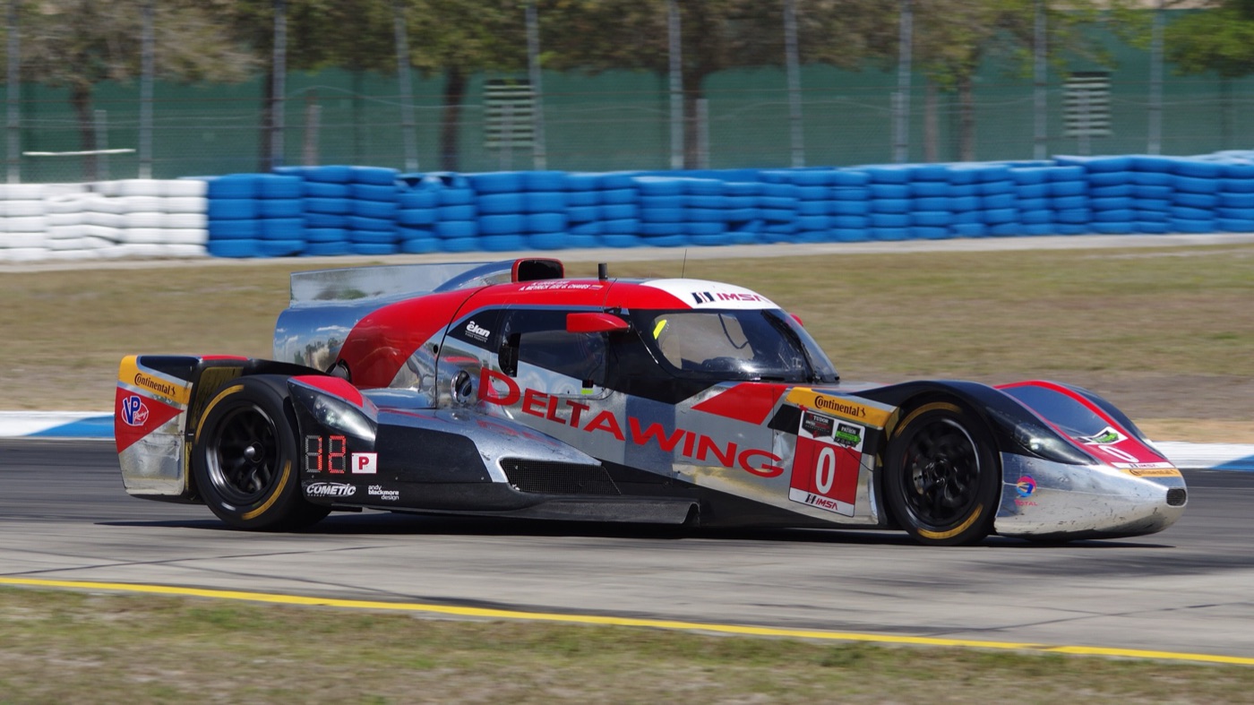 Silver, red and black DeltaWing coupe number 0 on track at Sebring with blue tyre barriers behind
