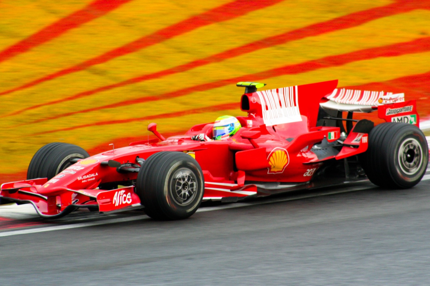 Felipe Massa in the red Ferrari F2008, yellow and green helmet visible, on the track at Interlagos in front of a red and yellow painted run-off