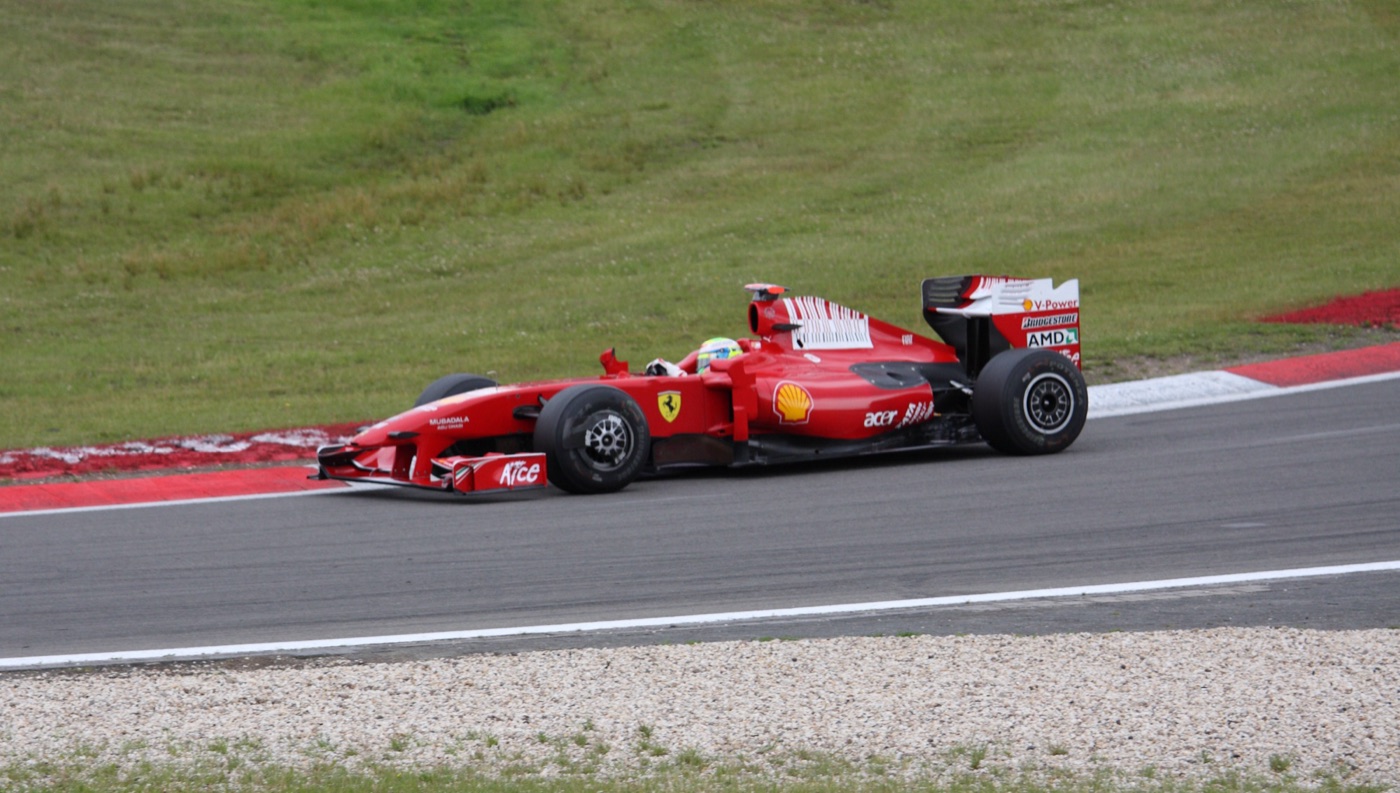 Red Ferrari F60 Formula One car with Felipe Massa’s yellow and green helmet visible, on track beside a grass bank at the Nürburgring