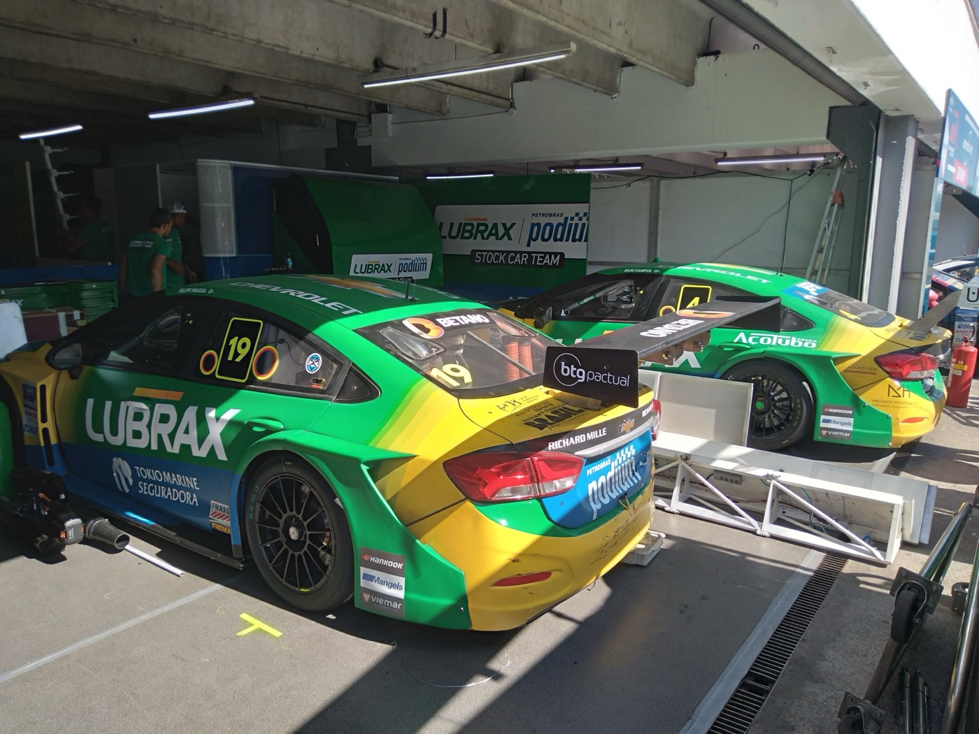 Green and yellow Lubrax Chevrolet Stock Car number 19 parked in a pit garage