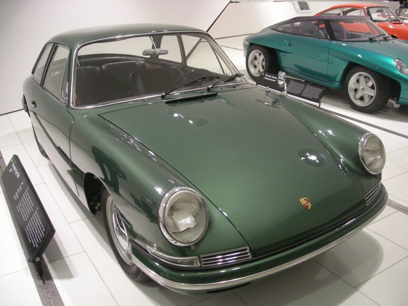 Dark green Porsche Type 754 T7 four-seat prototype coupé with round headlamps, on display in a white museum hall