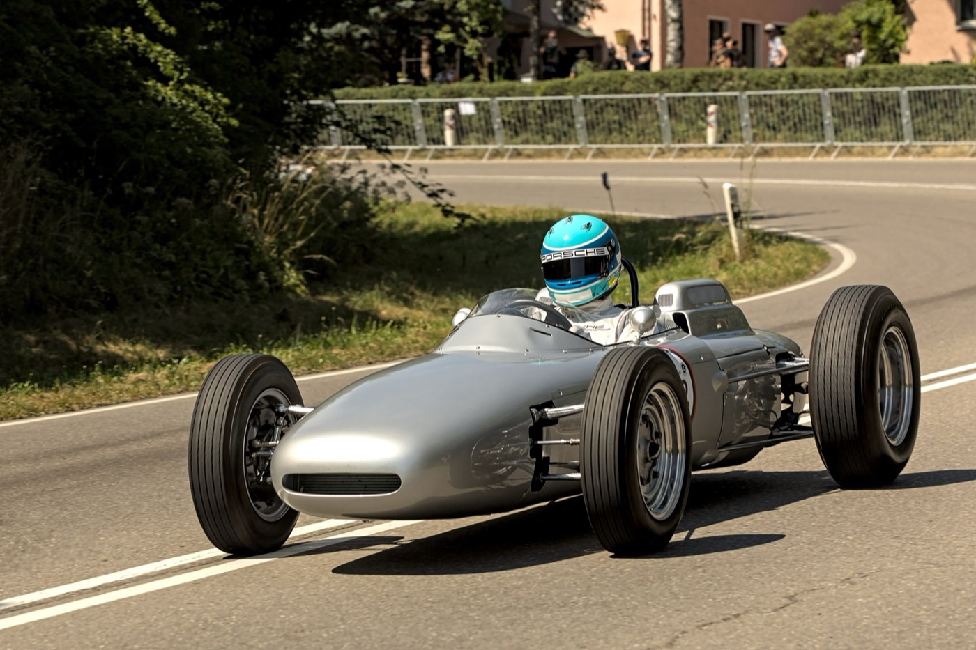 Silver Porsche 804 Formula One car with open wheels, driven through a bend by a driver in a light blue Porsche helmet