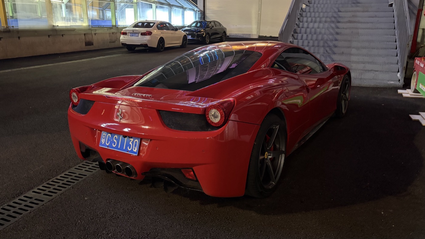 Rear three-quarter view of a red Ferrari 458 Italia at night showing its three central exhaust pipes and the glass engine cover